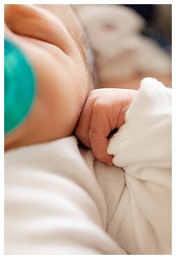 newborn with a hospital pacifier, highlighting his relaxed hand resting near his cheek