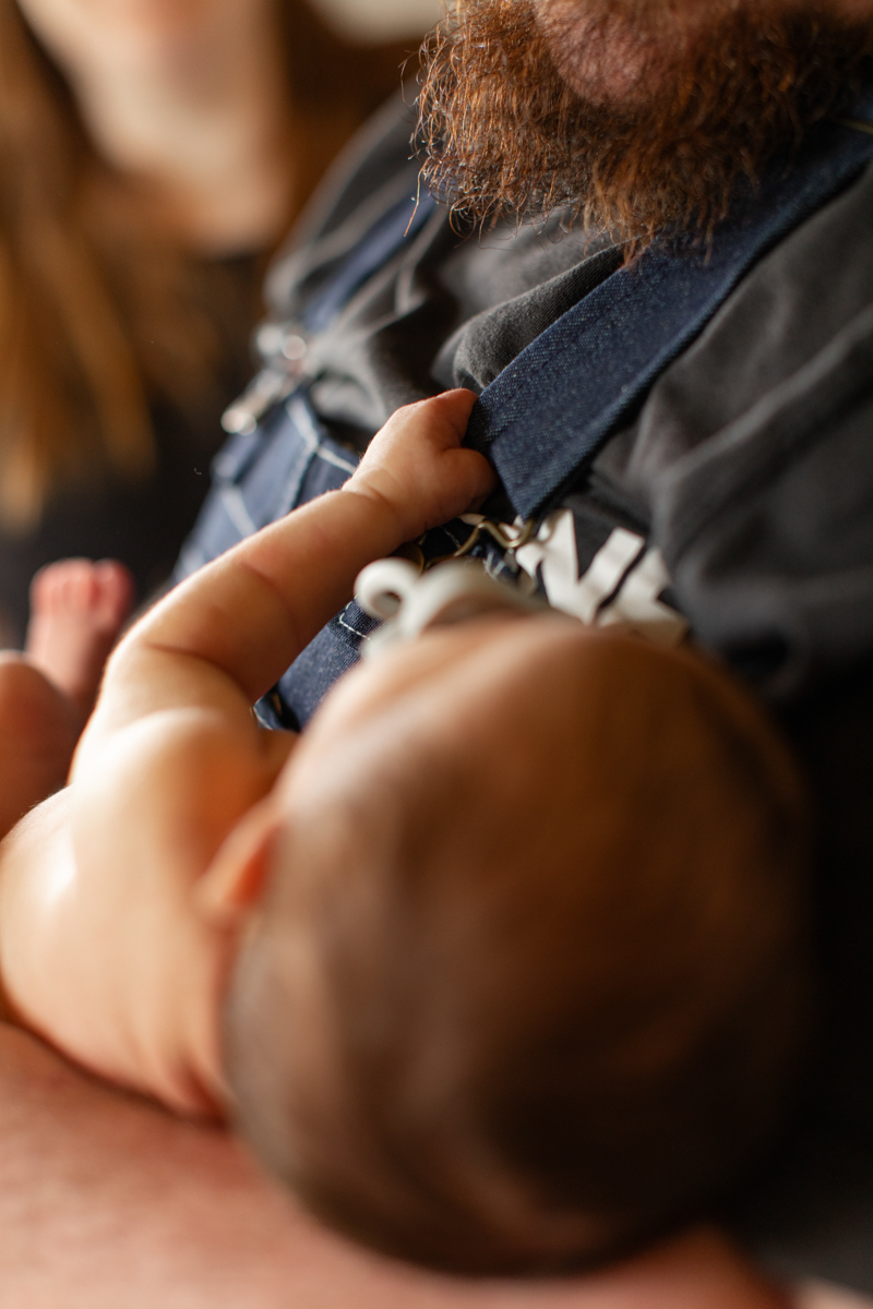 Newborn baby boy is gripping tightly onto dads overalls
