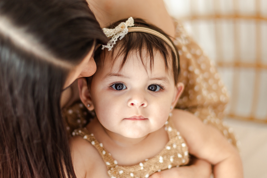 A tender moment between mom and baby, as mom whispers in baby's ear and kisses their cheek, both in an intimate, loving pose.