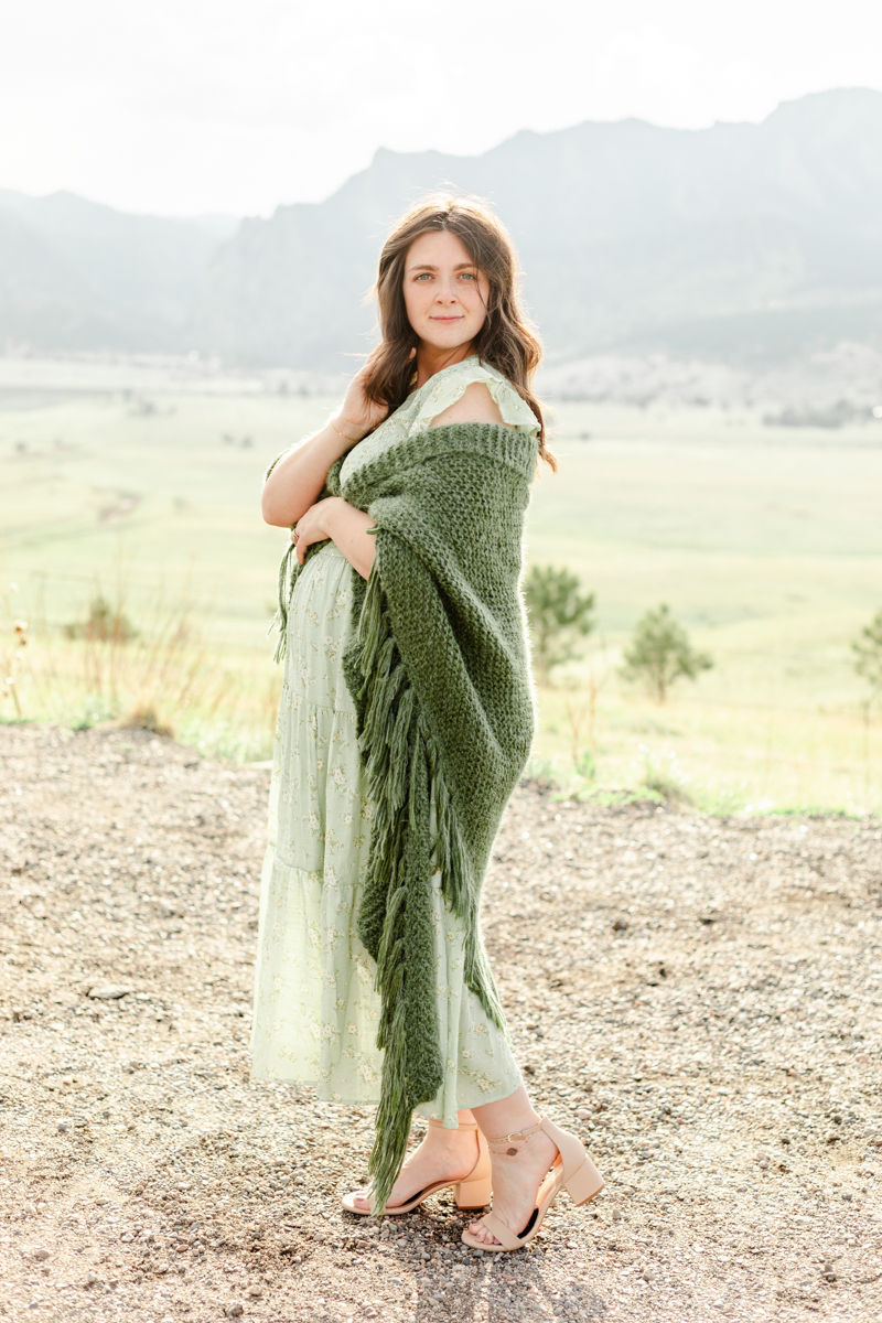 Pregnant woman in long, light green, floral dress with a dark green shawl.