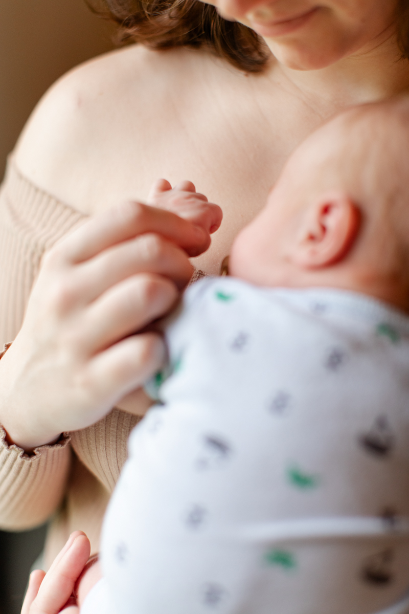 Newborn laying on mothers chest while mother holds his tiny hand