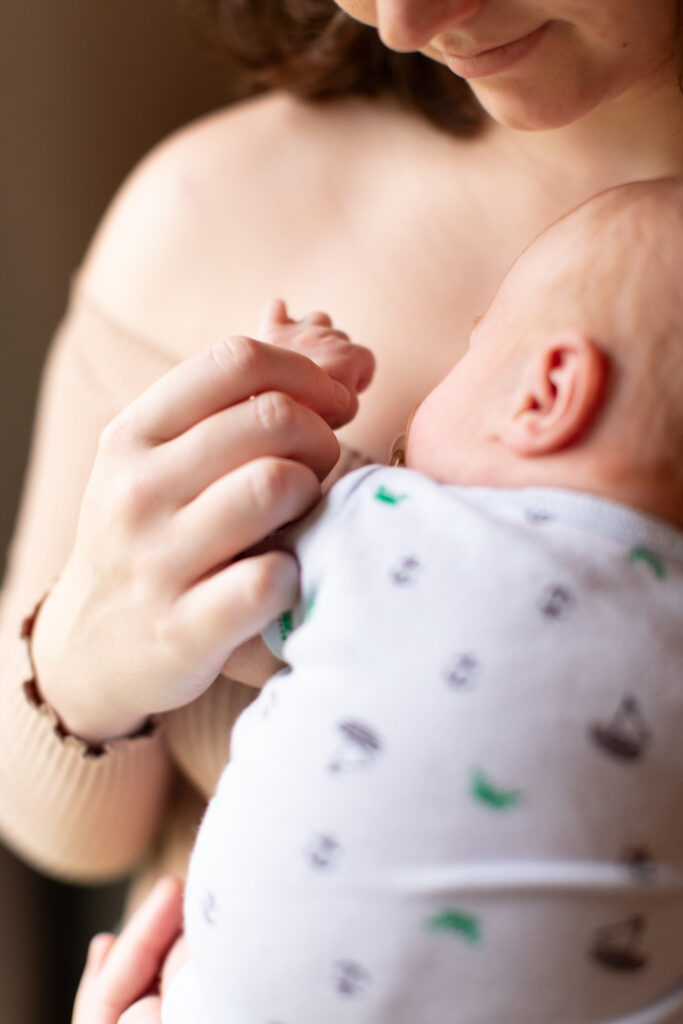 tender newborn moment, a close-up of mother and baby holding hands while the baby rests on her chest