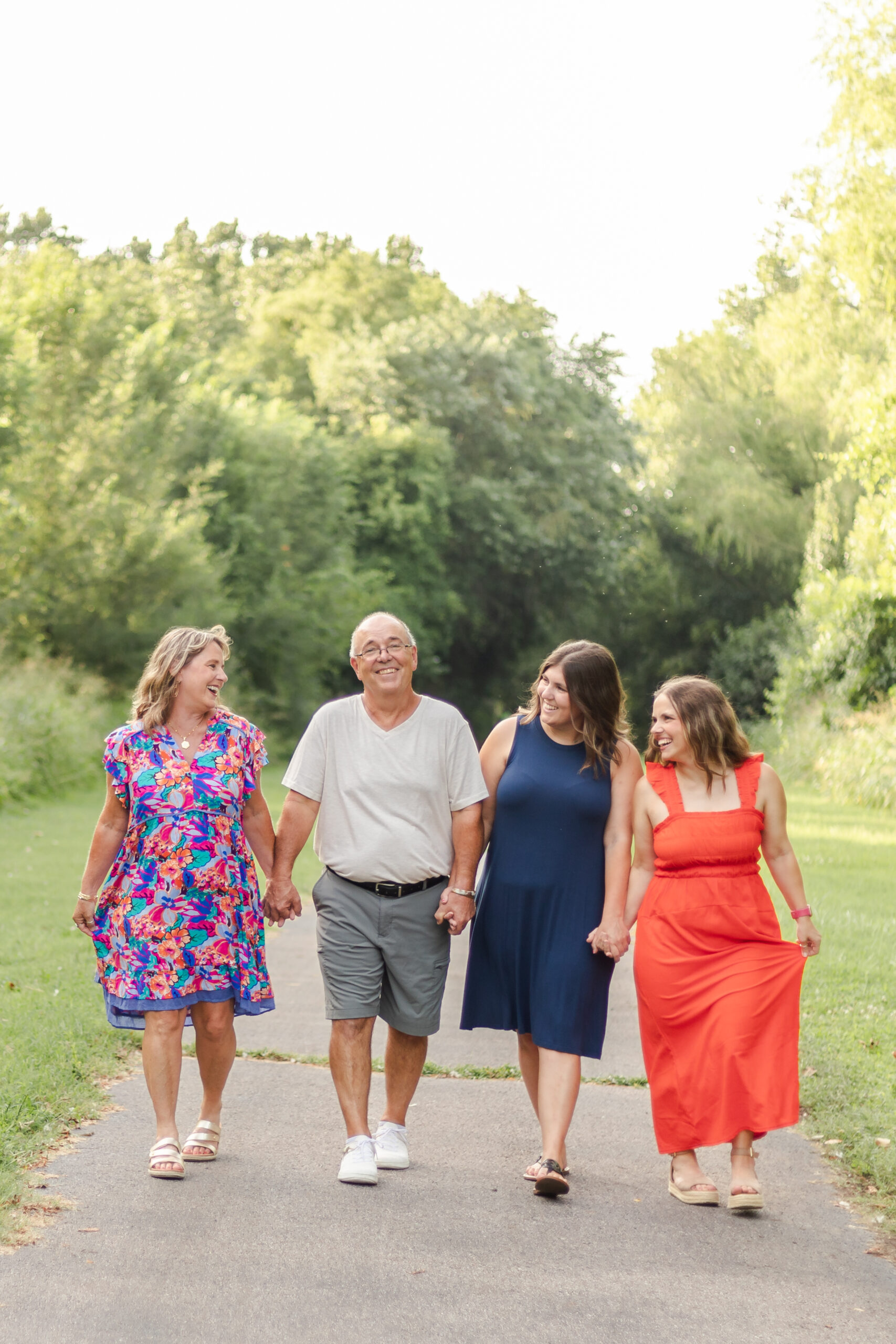 family of four walking down wooded path, hand in hand laughing