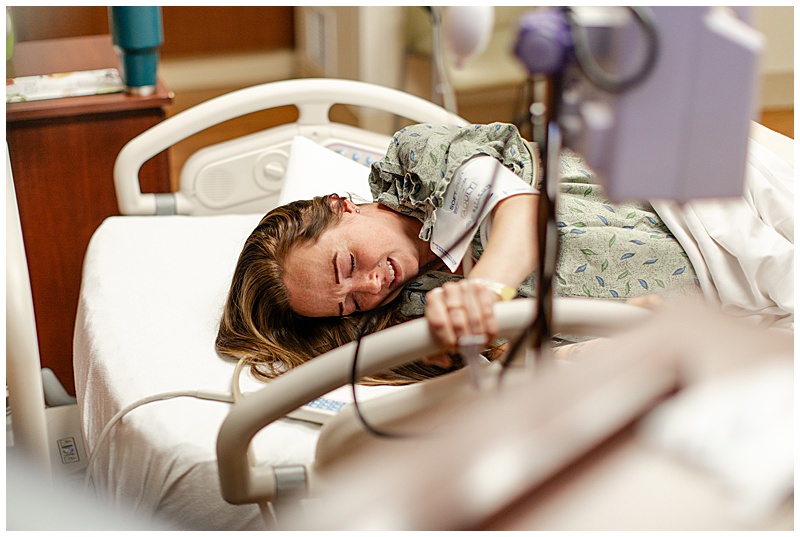 mother in labor laying down on hospital bed, gripping hand rail through contraction.