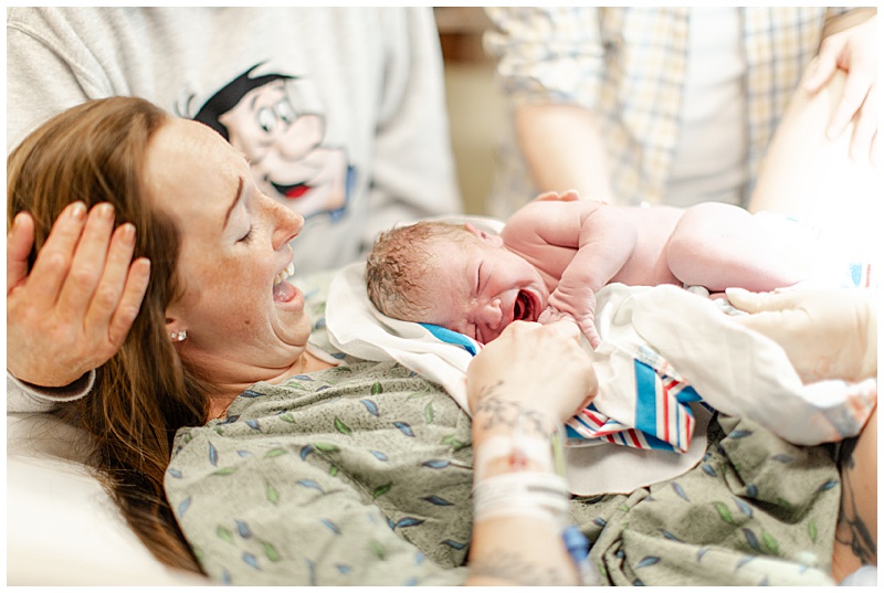 Mother emotionally holding newborn on chest for the first time after delivery. Newborns mouth is wide open in a cry