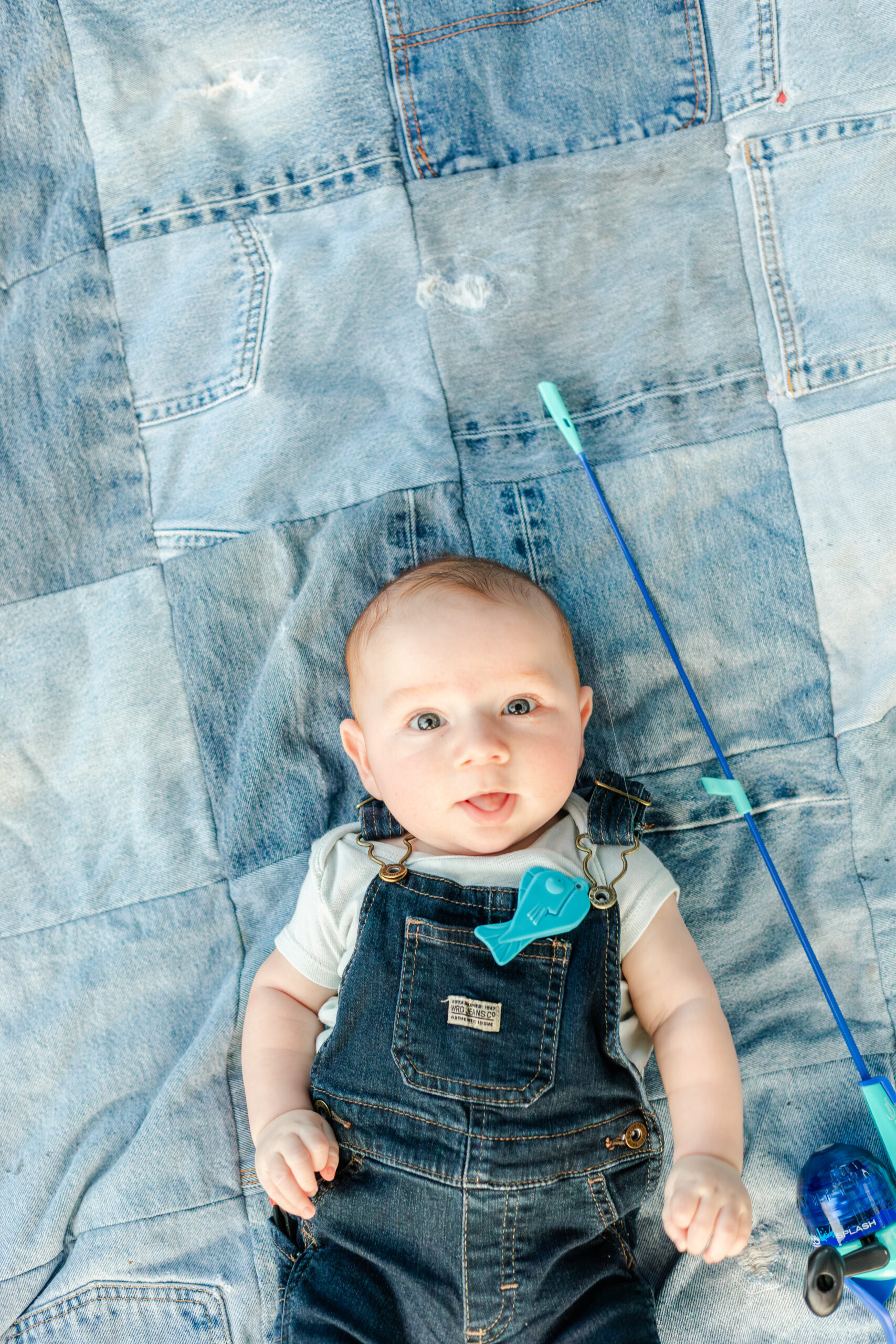 baby milestone laying on denim blanket with fishing pole