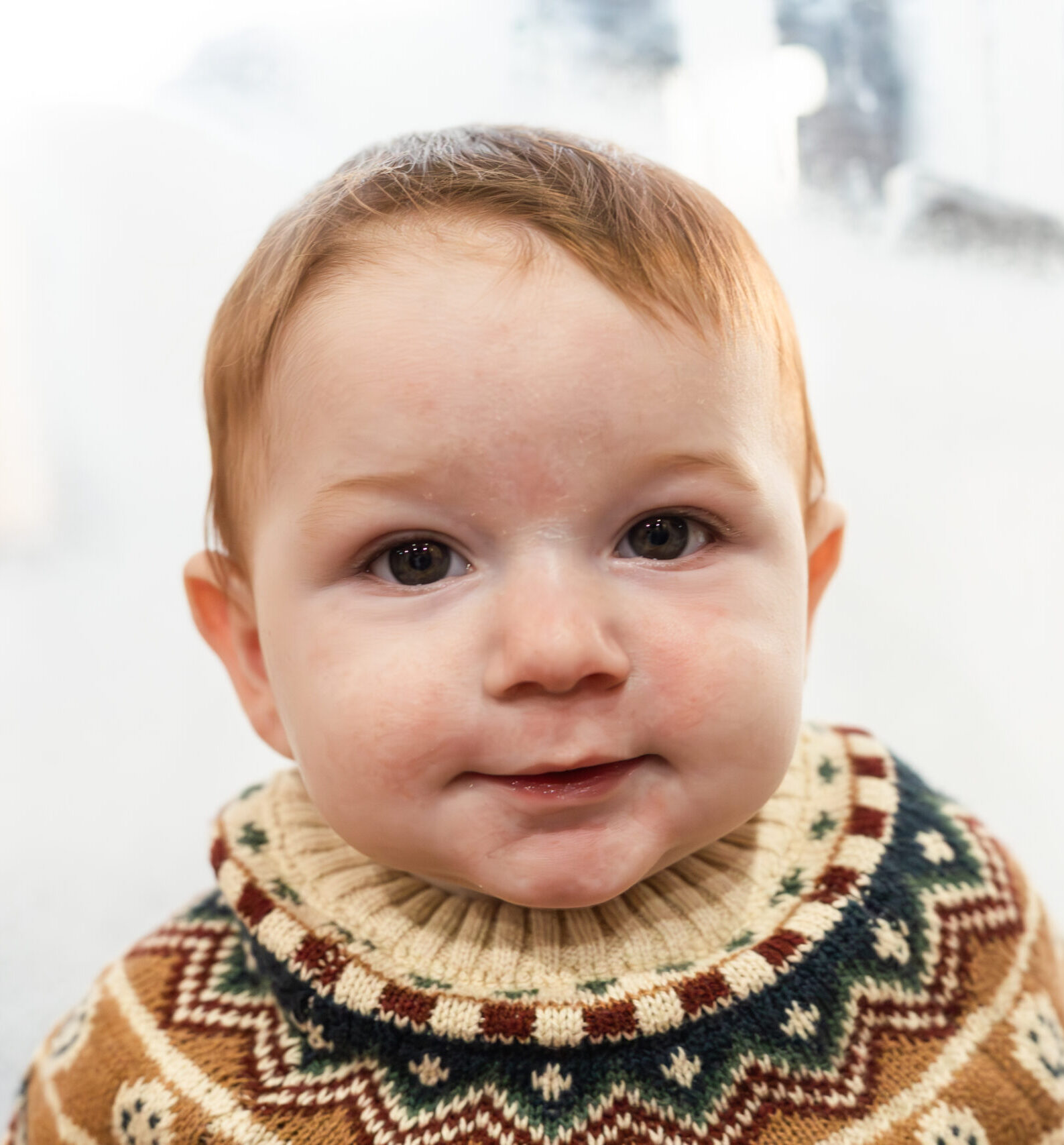 6 month old in a winter sweater smiling at camera in front of frosted window