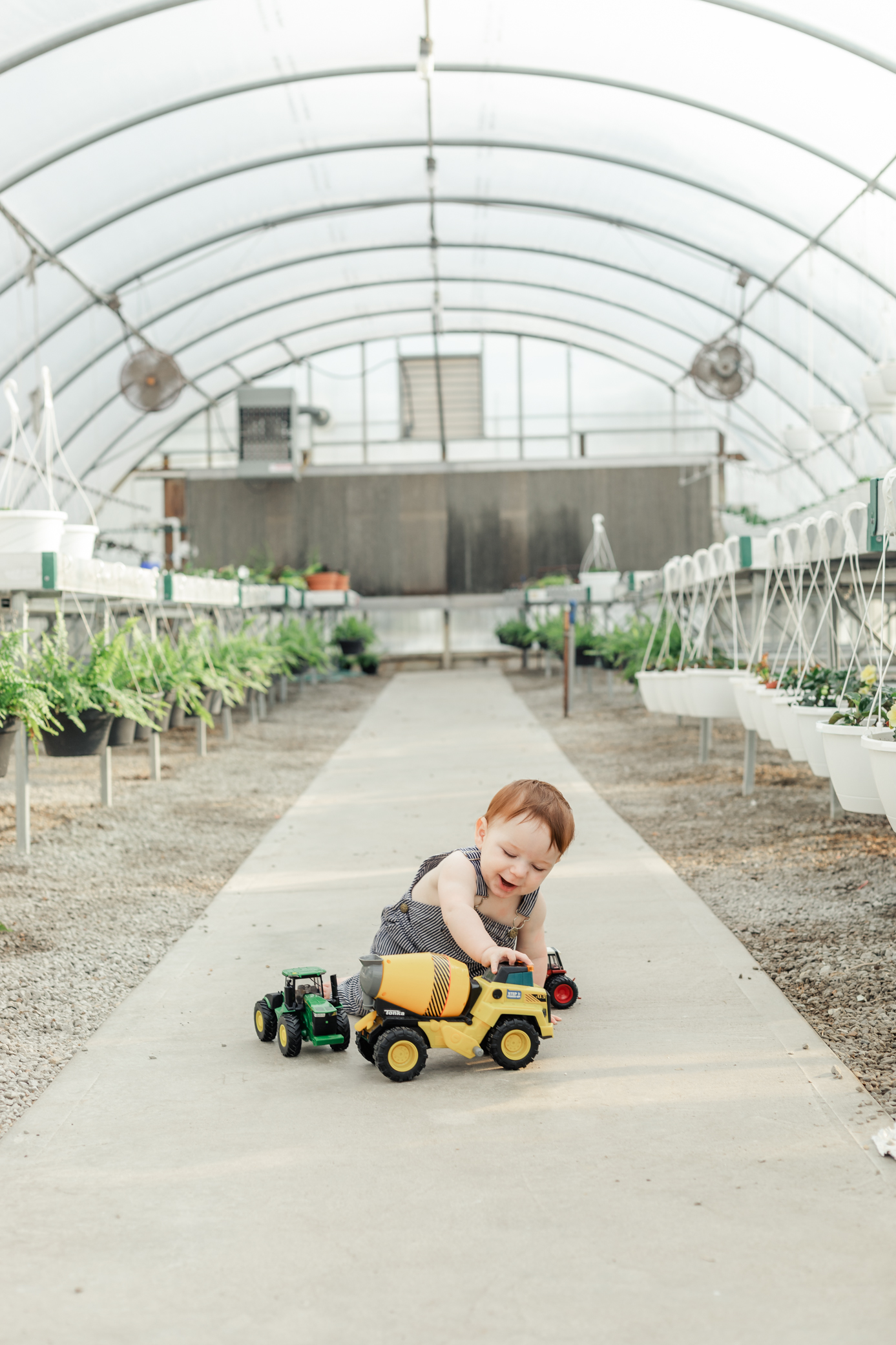 9 month old playing with trucks in a greenhouse, wearing blue overalls